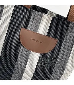 Close-up of vertical striped canvas tote bag featuring a premium brown leather logo patch