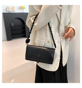 Détail d'un sac porté épaule noir mat avec bandoulière tressée sur veste en tweed