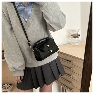 Detail of vintage black crossbody bag with gold buckle on a minimalist outfit background