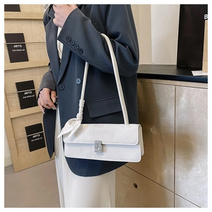 Close-up of a white baguette bag featuring a diamond buckle and decorative silk scarf strap