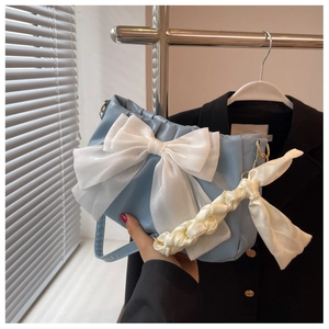 Detail of light blue shoulder bag featuring a large white organza bow and woven silk handle
