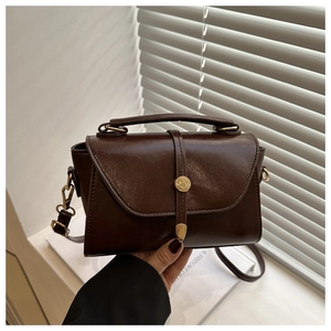 Close-up of a dark brown glossy leather handbag with gold hardware and top handle