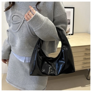 Glanzende zwarte hobo tas gedragen met grijze outfit in modern huiselijk decor