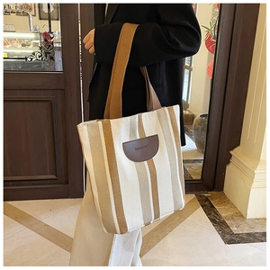 Detail of striped canvas tote with brown leather logo patch and wide strap