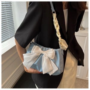 Detail of light blue handbag featuring a large white bow and woven satin shoulder strap