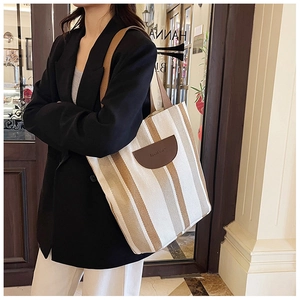 Detail of striped canvas tote bag featuring premium leather logo patch and wide shoulder strap