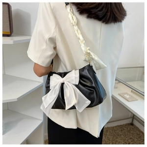 Close-up of black ruched shoulder bag with oversized white bow and woven fabric strap