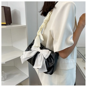 Detail of black pleated cloud bag featuring large white bow and woven ribbon strap
