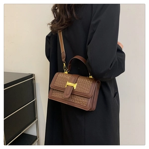 Détail d'un sac à main marron tressé avec fermoir en H doré porté par un modèle