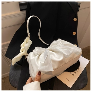 Detail of white satin shoulder bag with a large bow and silk scarf on a black chair