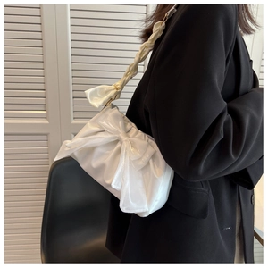 Detail of white satin shoulder bag featuring a large bow and twisted woven strap texture
