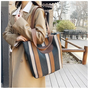 Outdoor view of a large striped knit tote bag styled with a khaki trench coat
