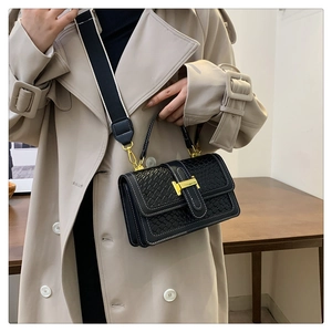 Détail d'un sac à main noir tressé avec boucle dorée et large bandoulière rayée