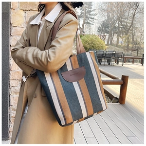 Detail of striped canvas tote with embossed leather brand patch and fabric strap
