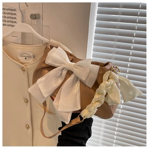 Detail of light brown cloud bag with large white mesh bow and pleated woven handle