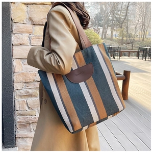 Detailed side view of a large striped canvas tote bag with brown woven shoulder strap