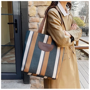 Detail shot of a striped canvas tote bag with brown leather logo patch and wide shoulder strap