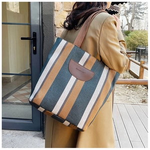 Detailed close-up of striped canvas tote bag featuring premium leather patch and sturdy strap