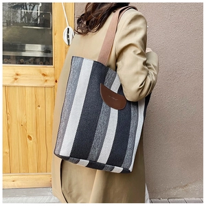 Detail of vertical striped tote bag showing brown leather logo patch and woven texture