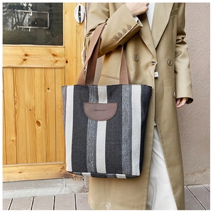 Detail of striped canvas tote bag with brown leather patch and woven handles on a coat