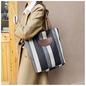 Detail of striped canvas tote bag with brown leather patch and khaki shoulder strap