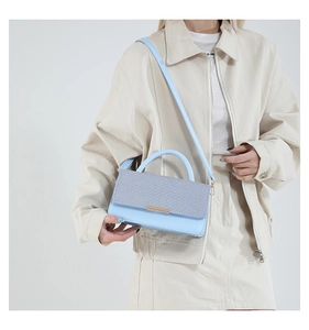 Détail du sac bandoulière bleu clair avec rabat tissé et boucle dorée sur un mannequin