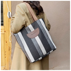 Detail showing striped tote bag with leather logo patch and brown woven shoulder strap