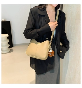 Detail of khaki PU leather bucket bag featuring a brown plush ball and gold metallic clasp