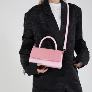 Sac à main rose avec rabat texturé et boucle dorée porté par un mannequin