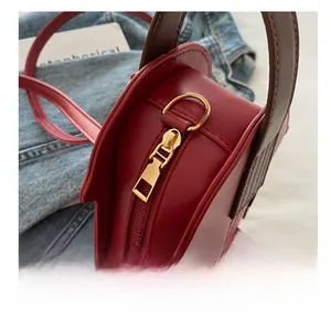 Detail of golden metal zipper and D-ring hardware on red leather crossbody bag