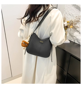 Detail of black matte leather bucket bag with a cute brown plush charm on a model