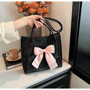 Detail der schwarzen Shopper-Tasche mit rosa Schleife und geflochtenem Griff auf Tisch