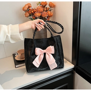 Detail der schwarzen Leder-Tote-Bag mit großer rosa Schleife und geflochtenen Henkeln auf Marmor