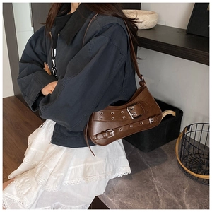 Detail of dark brown leather underarm bag with metal eyelets and decorative straps
