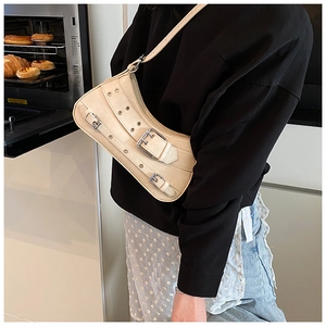Side view of a cream half-moon crossbody bag featuring silver eyelets and buckles