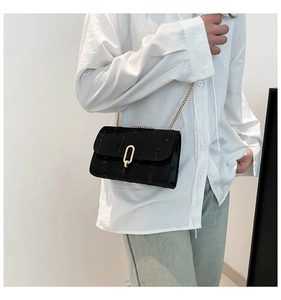 Detail of black textured crossbody bag with gold chain strap on a casual outfit