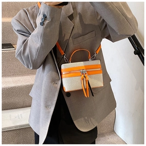 Détail du sac boîte en toile contrastée avec garniture en cuir orange et pompons longs