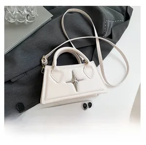 Détail du sac à bandoulière en cuir crème avec étoile argentée sur blazer gris foncé