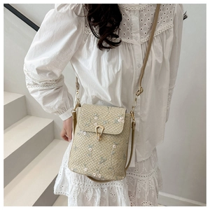 Close-up of woven straw square bag with delicate floral embroidery and gold metal clasp