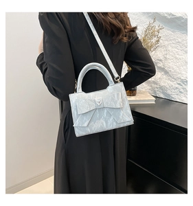 Détail du sac à main bleu clair avec nœud papillon et texture brillante plissée