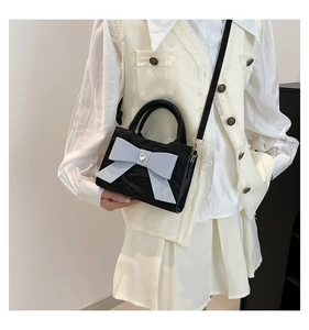 Détail du sac à main noir brillant avec grand nœud bleu clair et boucle en forme de cœur