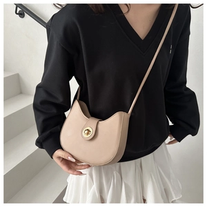 Detail of beige crescent saddle bag with gold circular twist lock on model in white setting