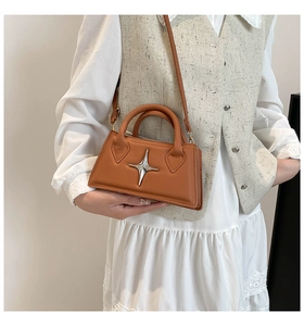 Détail d'un mini sac trapèze marron avec un emblème en métal argenté et une bandoulière