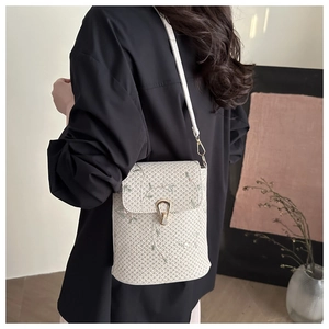 Detailed view of cream woven crossbody bag with delicate floral embroidery and gold metal lock