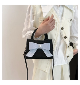 Détail d'un sac à main noir avec grand nœud et boucle coeur argentée sur gilet en tweed