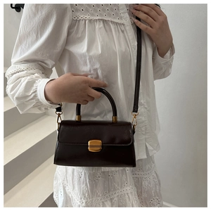 Detail of vintage dark brown faux leather crossbody bag with gold buckle on white lace outfit
