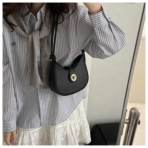 Model wearing a black crescent hobo bag with a gold metal clasp and leather strap