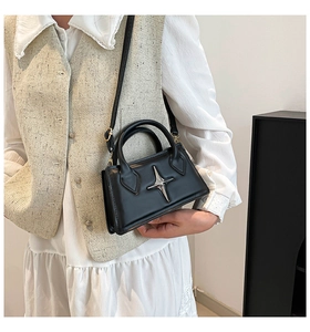 Détail d'un sac bandoulière noir mat avec étoile argentée porté sur un gilet en tweed