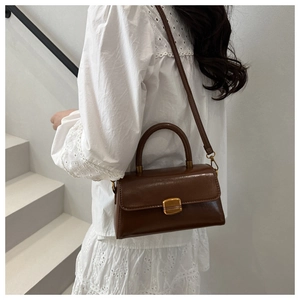 Close-up of vintage brown leather handbag with gold metal clasp on a white lace dress