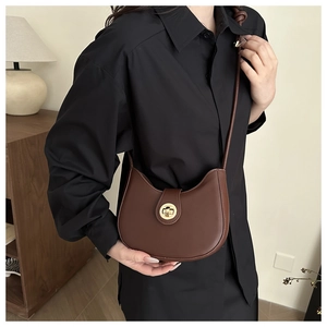 Detail of a deep brown leather half-moon shoulder bag with a gold metal twist lock